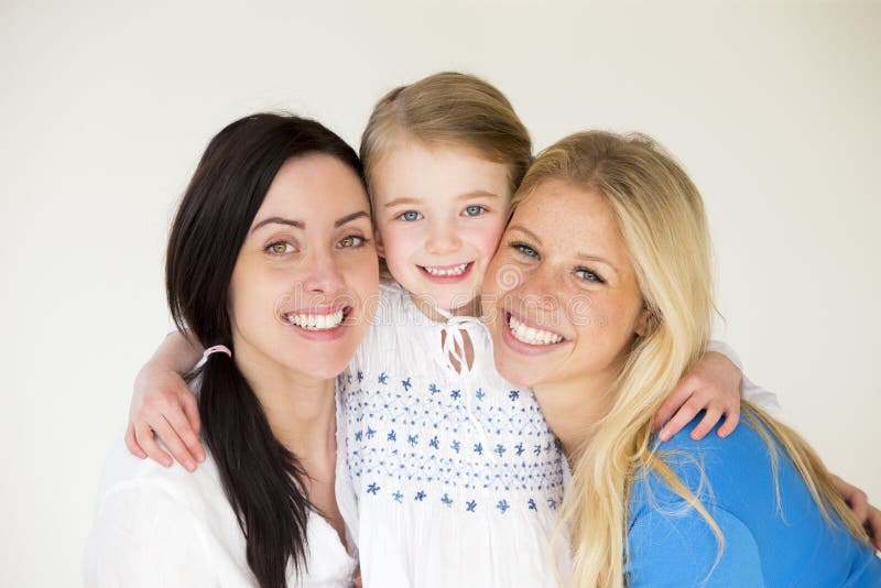 Same sex female couple posing with their daughter in front of a plain background. Same sex female couple posing with their daughter in front of a plain background