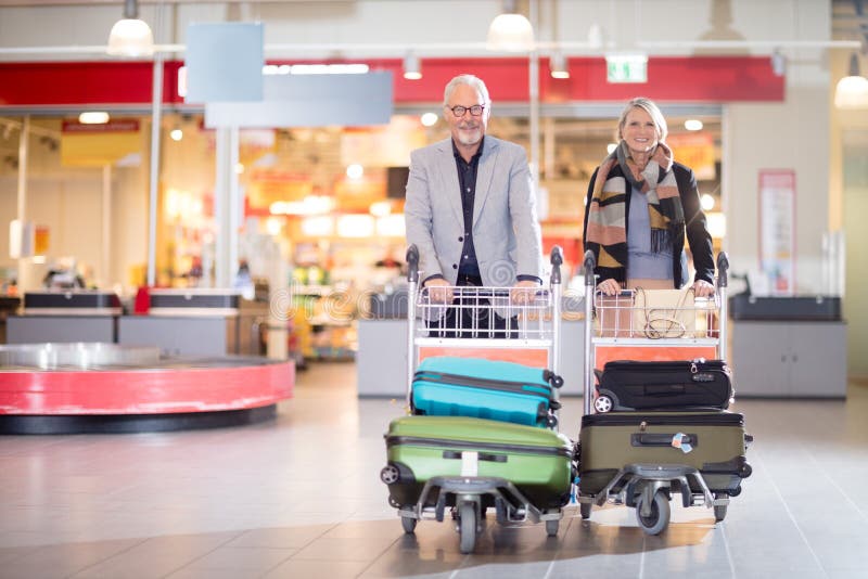 Ajouter supérieurs heureux d'affaires au bagage dans des chariots à l'aéroport images libres de droits Ajouter supérieurs heureux d'affaires au bagage dans des chariots à l'aéroport images libres de droits
