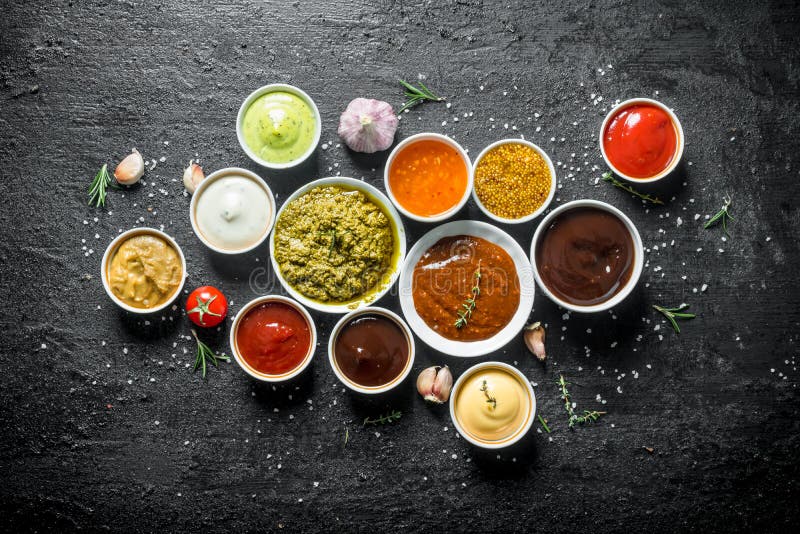 Set of sauces - tomato sauce, pesto, mustard, barbecue sauce, guacomole, mayonnaise. On black rustic background. Set of sauces - tomato sauce, pesto, mustard, barbecue sauce, guacomole, mayonnaise. On black rustic background