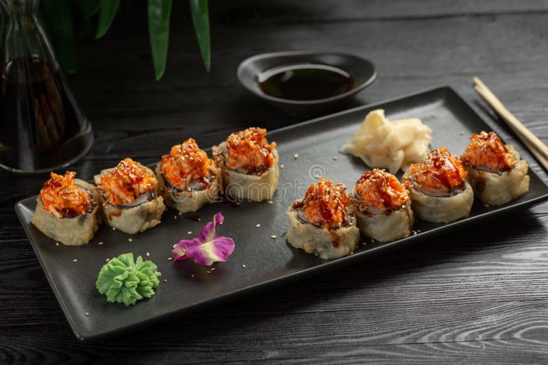 Ajuste dos rolos de sushi em uma placa retangular preta em um fundo de madeira preto foto de stock Ajuste dos rolos de sushi em uma placa retangular preta em um fundo de madeira preto foto de stock