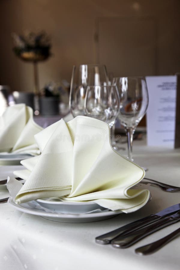 Closeup of and elegant table setting with cutlery and glasses for a variety of courses and decoratively folded cream linen napkin. Closeup of and elegant table setting with cutlery and glasses for a variety of courses and decoratively folded cream linen napkin