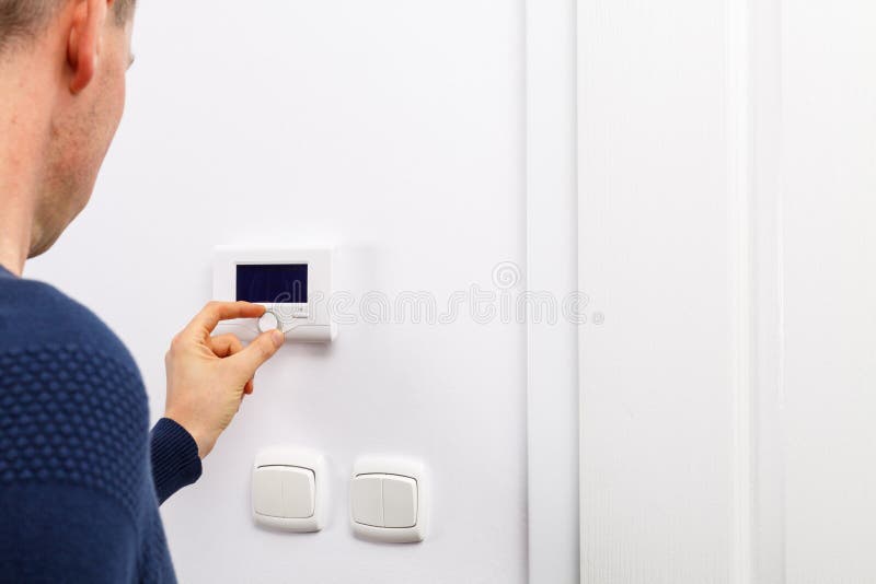 Men regulate temperature on control panel of central heating at wall in living room. Men regulate temperature on control panel of central heating at wall in living room.