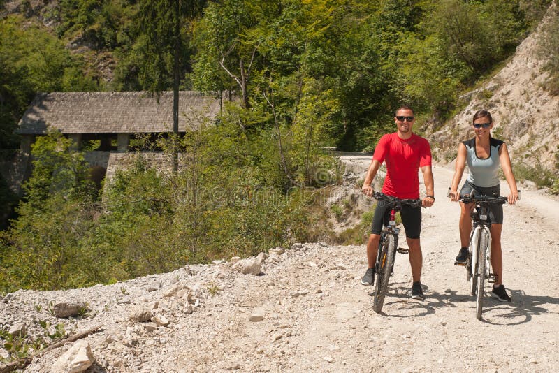 Aktive junge Paare, die in Wald an einem heißen Sommertag radfahren lizenzfreie stockfotografie Aktive junge Paare, die in Wald an einem heißen Sommertag radfahren lizenzfreie stockfotografie
