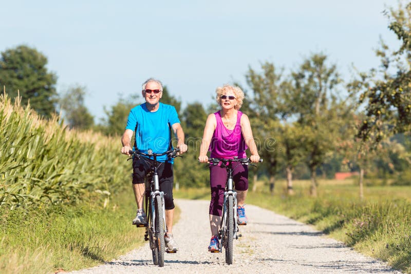 Full length front view of an active senior couple enjoying retirement while riding bicycles in a sunny day of summer in the countryside. Full length front view of an active senior couple enjoying retirement while riding bicycles in a sunny day of summer in the countryside