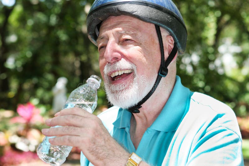 Active senior man wearing a bicycle helmet stops to drink bottled water. Active senior man wearing a bicycle helmet stops to drink bottled water.