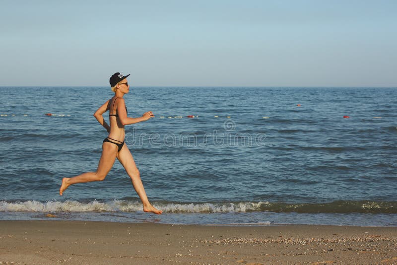 Aktywny sporty kobieta bieg wzdłuż ocean kipieli wodnym basenem utrzymywać napad i zdrowie Zmierzchu piaska plaży czarny tło z zdjęcie stock Aktywny sporty kobieta bieg wzdłuż ocean kipieli wodnym basenem utrzymywać napad i zdrowie Zmierzchu piaska plaży czarny tło z zdjęcie stock