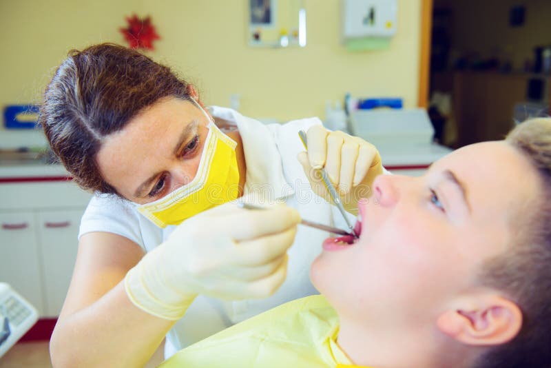 Al dentista de sexo femenino trata al muchacho fotografía de archivo libre de regalías Al dentista de sexo femenino trata al muchacho fotografía de archivo libre de regalías