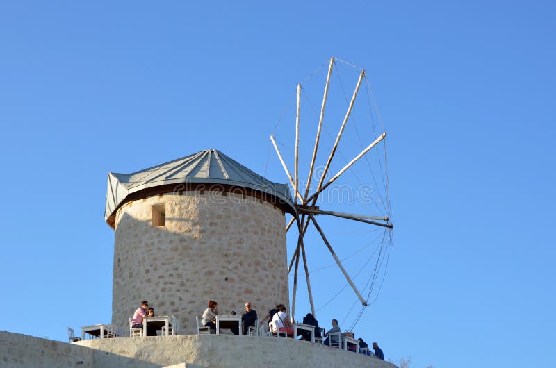 Alacati, Smirne, Turchia: 13 ottobre 2013: Vista di vecchio wildmill in Alacati La gente sta godendo del tempo in un caffè vicino fotografie stock libere da diritti Alacati, Smirne, Turchia: 13 ottobre 2013: Vista di vecchio wildmill in Alacati La gente sta godendo del tempo in un caffè vicino fotografie stock libere da diritti