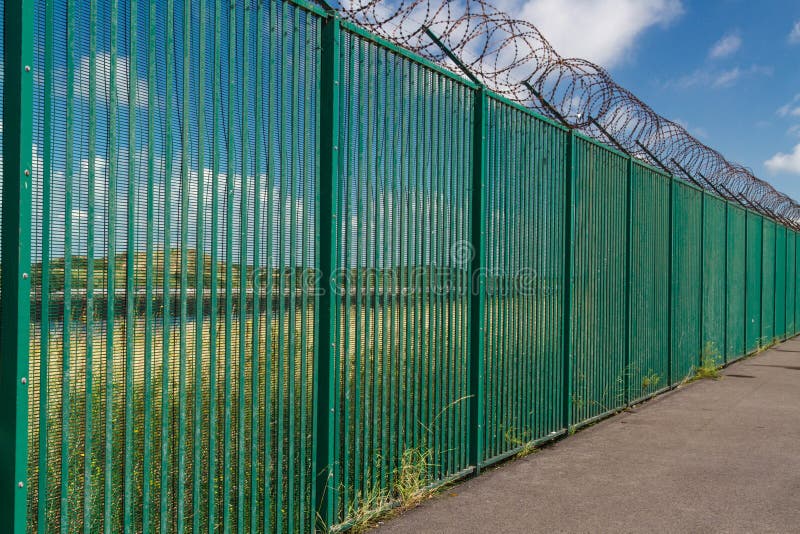 Alambre de la maquinilla de afeitar encima de la cerca verde que guarda la terminal de transbordadores francesa imagenes de archivo Alambre de la maquinilla de afeitar encima de la cerca verde que guarda la terminal de transbordadores francesa imagenes de archivo