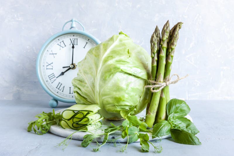 Alarm clock, Asparagus, microgreens, cucumber and cabbage - fresh green vegetables. Ketogenic diet, intermittent fasting, weight