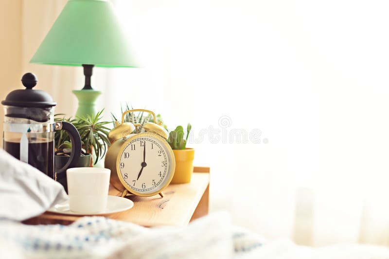 Alarm clock and coffee cup at bed in sunny room. Easy morning start, positive day beginning, waking up, new day concept