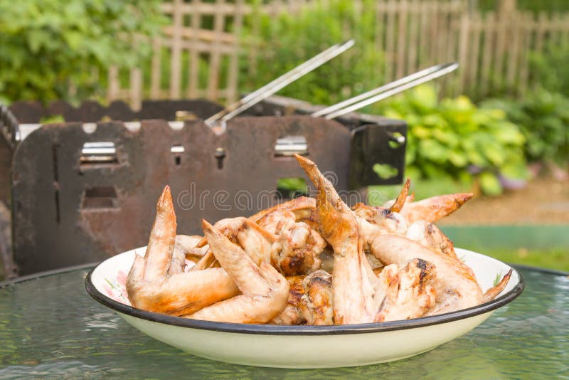 Alas de pollo asadas a la parrilla en un plato al lado de la parrilla de la barbacoa en un patio trasero en verano imagen de archivo Alas de pollo asadas a la parrilla en un plato al lado de la parrilla de la barbacoa en un patio trasero en verano imagen de archivo