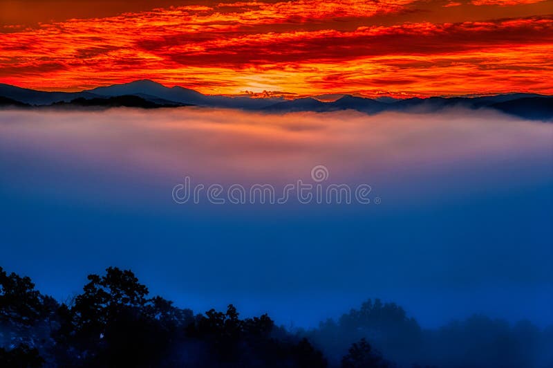 A photograph of a cold October dawn from the foothills near the Great Smoky Mountains National Park.  The cold air had forced clouds down to the ground, so that only the tips of mountains could be seen.  An orange sky blends beautifully with the cool blue of the fog/clouds. A photograph of a cold October dawn from the foothills near the Great Smoky Mountains National Park.  The cold air had forced clouds down to the ground, so that only the tips of mountains could be seen.  An orange sky blends beautifully with the cool blue of the fog/clouds