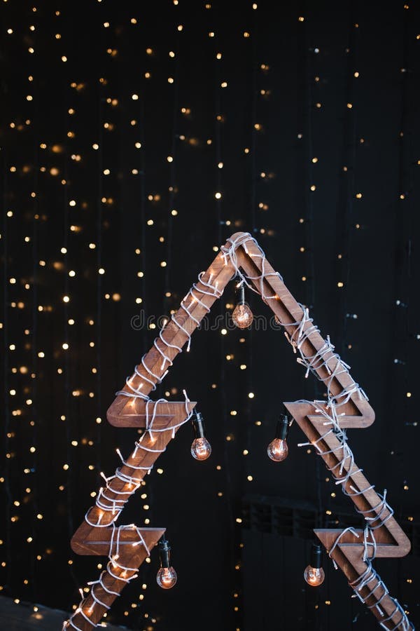Albero di Natale di legno alternativo Un albero fatto a mano del nuovo anno con la lampadina sul fondo nero delle luci della ghir fotografia stock Albero di Natale di legno alternativo Un albero fatto a mano del nuovo anno con la lampadina sul fondo nero delle luci della ghir fotografia stock