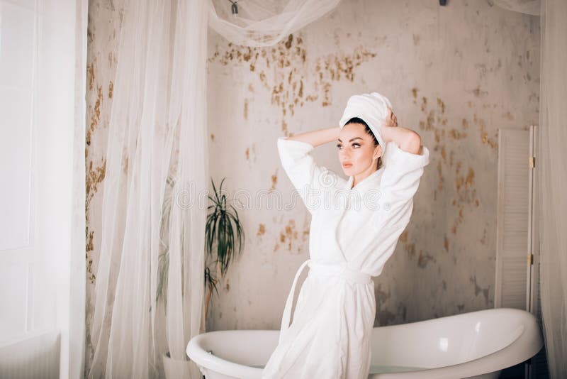 Albornoz blanca que lleva y toalla de la muchacha atractiva en la cabeza en cuarto de baño imagen de archivo Albornoz blanca que lleva y toalla de la muchacha atractiva en la cabeza en cuarto de baño imagen de archivo