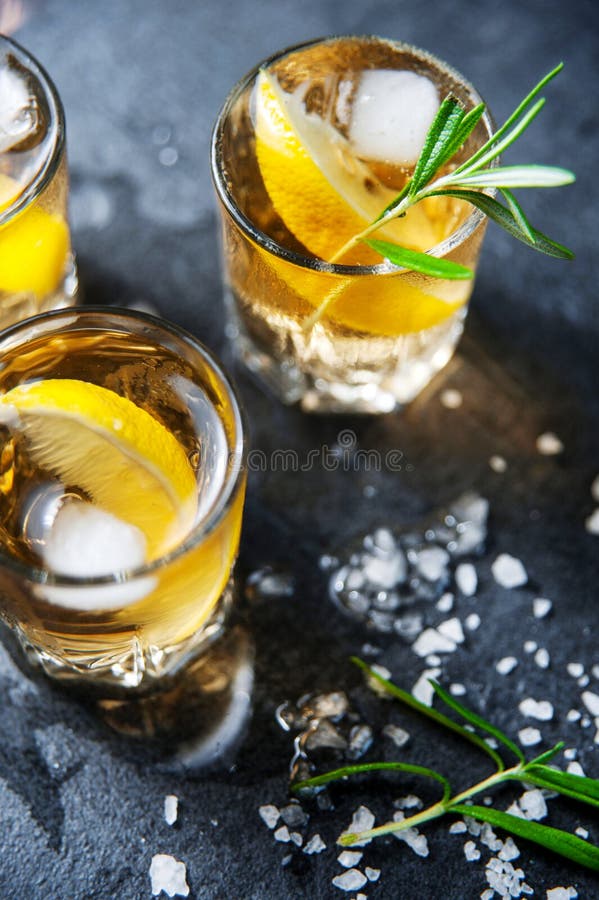 Alcohol cocktail with ice and smoking rosemary on dark table lemon