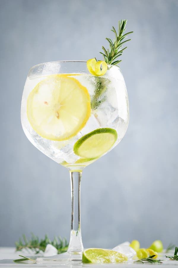 Alcohol drink, gin tonic cocktail, with lemon, lime, rosemary and ice on light background, copy space. Iced drink