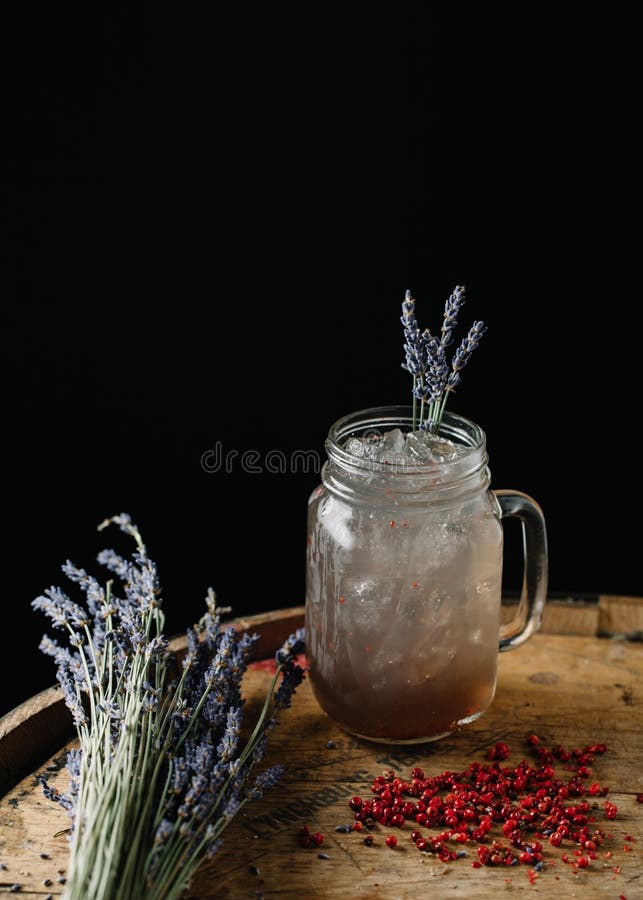 An alcoholic beverage garnished with lavender and peppercorns. An alcoholic beverage on dark background stock photo An alcoholic beverage garnished with lavender and peppercorns. An alcoholic beverage on dark background stock photo