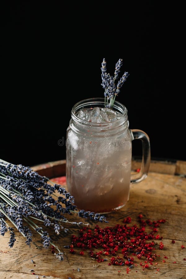 An alcoholic beverage garnished with lavender and peppercorns. An alcoholic beverage on dark background stock image An alcoholic beverage garnished with lavender and peppercorns. An alcoholic beverage on dark background stock image