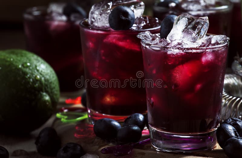 Alcoholic cocktail with liqueur, blueberry, lime juice, crushed ice, bar tools on black background, selective focus