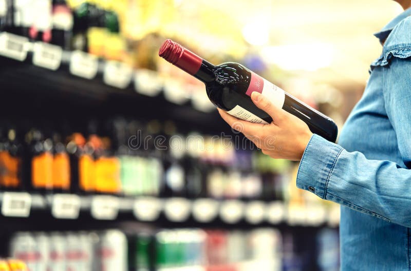 Alcoholplank in slijterij of supermarkt Vrouw die een fles rode wijn kopen en alcoholische dranken in winkel bekijken