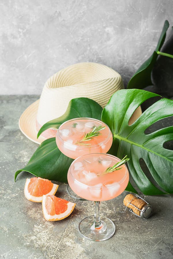 Alecrins e gelo da toranja da bebida em dois cálices de vidro elegantes no fundo das folhas e de chapéus verdes tropicais fotografia de stock royalty free Alecrins e gelo da toranja da bebida em dois cálices de vidro elegantes no fundo das folhas e de chapéus verdes tropicais fotografia de stock royalty free