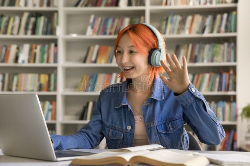 Alegre estudiante pelirroja con auriculares inalámbricos saludando con la mano imágenes de archivo libres de regalías