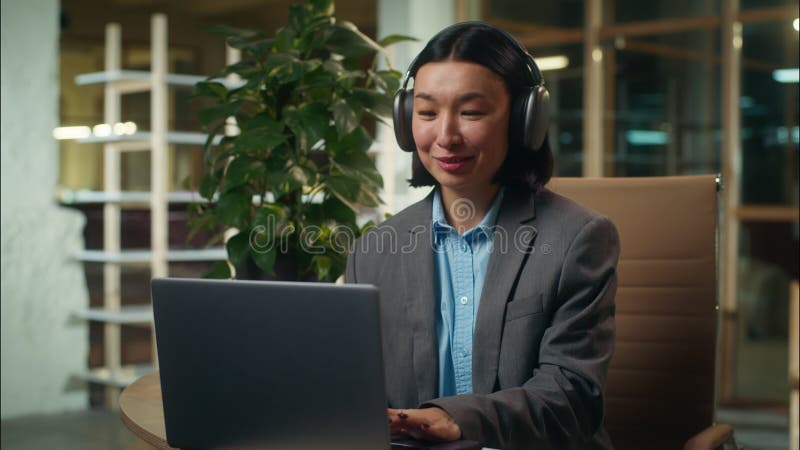 Alegre feliz mujer asiática coreana japonesa trabajando con música en el portátil en los auriculares chica de alegría femenina metrajes