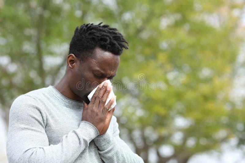 Allergic black man blowing on wipe in a park on spring season a sunny day. Allergic black man blowing on wipe in a park on spring season a sunny day
