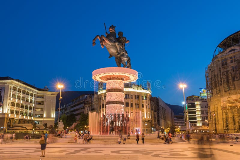 SKOPJE, MACEDONIA - JULY 17, 2015: Long exposure night scene of the people walking by the fountain with statue of Alexander the Great on top in the middle of the main square in downtown of capital city. SKOPJE, MACEDONIA - JULY 17, 2015: Long exposure night scene of the people walking by the fountain with statue of Alexander the Great on top in the middle of the main square in downtown of capital city.