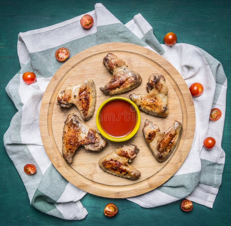 Ali di pollo arrostite con il tagliere piccante della salsa di peperoncino rosso sui pomodori ciliegia a strisce di un tovagliolo fotografie stock libere da diritti Ali di pollo arrostite con il tagliere piccante della salsa di peperoncino rosso sui pomodori ciliegia a strisce di un tovagliolo fotografie stock libere da diritti