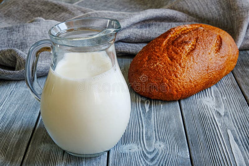Alimente simple pe lapte de masă într-un ulcior și pâine coaptă proaspătă. masă rustică alcătuită din scânduri. pânză royalty free stock images