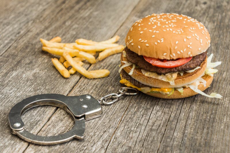 Handcuffs and hamburger on wooden background. Part of project Addicted. Handcuffs and hamburger on wooden background. Part of project Addicted