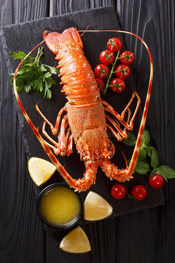 Expensive food: spiny boiled lobster with fresh tomato, lemon and melted butter close-up on black stone. Vertical top view from above. Expensive food: spiny boiled lobster with fresh tomato, lemon and melted butter close-up on black stone. Vertical top view from above