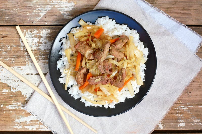 Alimento cinese con riso, la carota, il cavolo e la carne sulla banda nera su fondo di legno immagini stock libere da diritti Alimento cinese con riso, la carota, il cavolo e la carne sulla banda nera su fondo di legno immagini stock libere da diritti