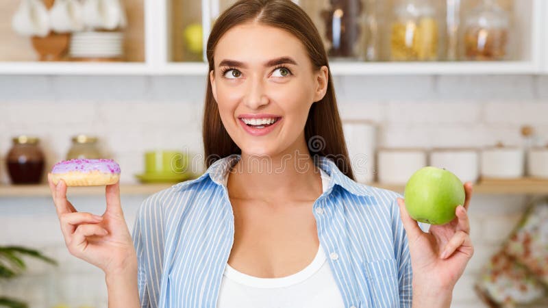 Alimento saud?vel Mulher que escolhe entre frutos e doces fotografia de stock Alimento saud?vel Mulher que escolhe entre frutos e doces fotografia de stock