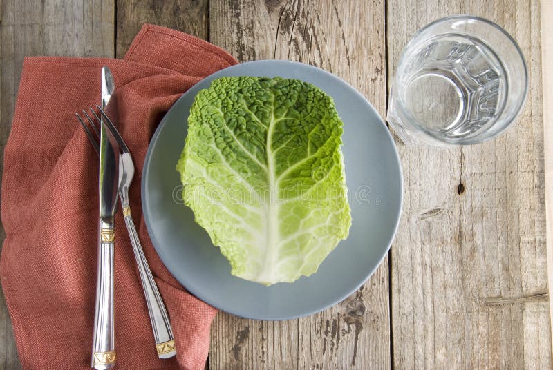 Alimento saudável e conceito de dieta Uma folha do brassica isolada na placa cinzenta, com forquilha e faca, sobre o fundo de mad foto de stock royalty free Alimento saudável e conceito de dieta Uma folha do brassica isolada na placa cinzenta, com forquilha e faca, sobre o fundo de mad foto de stock royalty free
