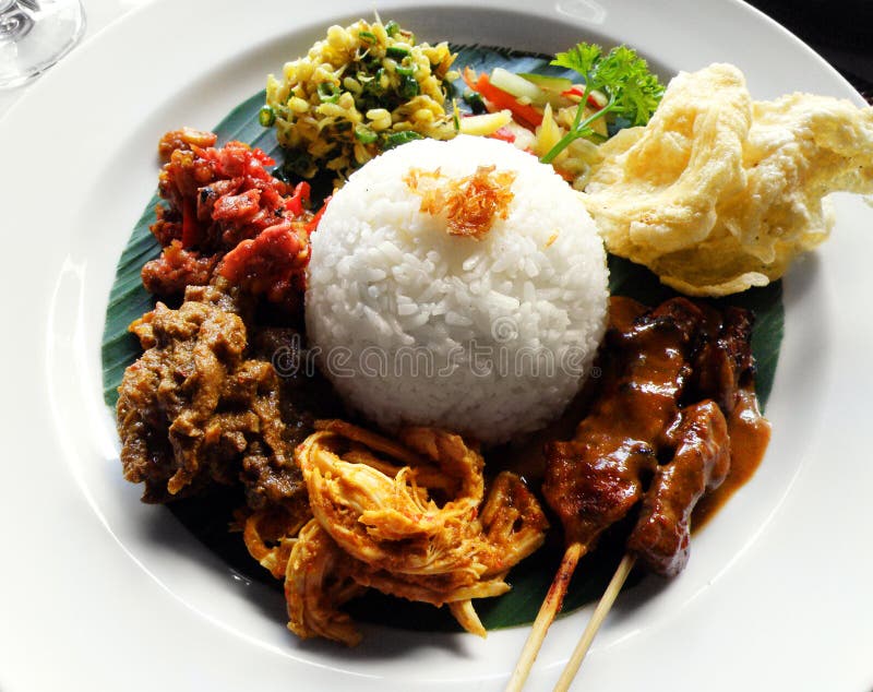 A photograph of a traditional asian ethnic main course meal of Nasi Campur, or white rice served with many assorted local side dishes of various spicy meats, fish and vegetables. also with tempeh, crispy local prawn crackers, krupuks. Delicious tasty and ethnic set meal and fast food cuisine very popular in Indonesia and bali, both with locals and tourists, common daily menu item. Photograph taken in restaurant cafe. Horizontal color photo, nobody in picture. Beautiful professional foods photography with natural day lighting. A photograph of a traditional asian ethnic main course meal of Nasi Campur, or white rice served with many assorted local side dishes of various spicy meats, fish and vegetables. also with tempeh, crispy local prawn crackers, krupuks. Delicious tasty and ethnic set meal and fast food cuisine very popular in Indonesia and bali, both with locals and tourists, common daily menu item. Photograph taken in restaurant cafe. Horizontal color photo, nobody in picture. Beautiful professional foods photography with natural day lighting.