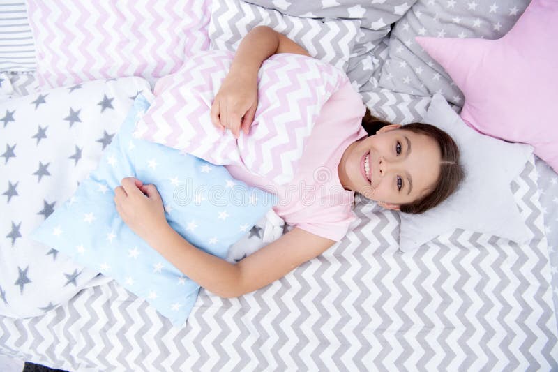 Aliste para dormir El niño feliz sonriente de la muchacha pone en cama con las almohadas asteroides y la tela escocesa linda en s