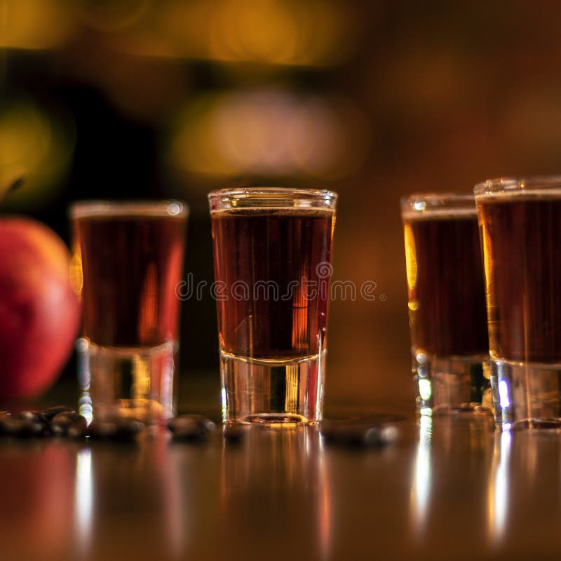 Alkohol shots coffee beans and apple on bar table on blurred background