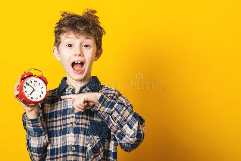 Allarme colpito dell'orologio della tenuta del ragazzo del bambino, spazio della copia Bambino isolato sopra fondo giallo Tempo p fotografie stock Allarme colpito dell'orologio della tenuta del ragazzo del bambino, spazio della copia Bambino isolato sopra fondo giallo Tempo p fotografie stock