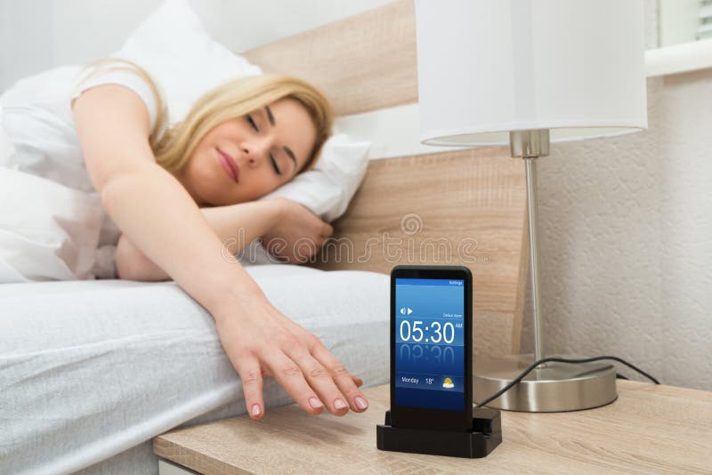Allarme sonnecchiante della donna sullo schermo del telefono cellulare fotografie stock libere da diritti Allarme sonnecchiante della donna sullo schermo del telefono cellulare fotografie stock libere da diritti
