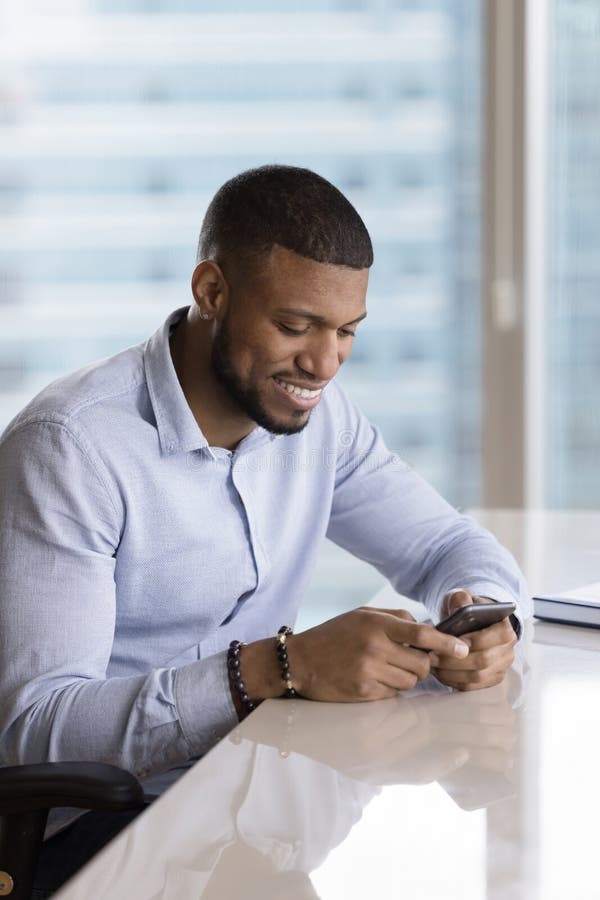 Allegro cliente soddisfatto che usa l'app di servizio online su smartphone seduto all'ufficio scrivendo chiacchiere per ottenere buone notizie dalla lettura di comunicazioni via Internet sullo schermo