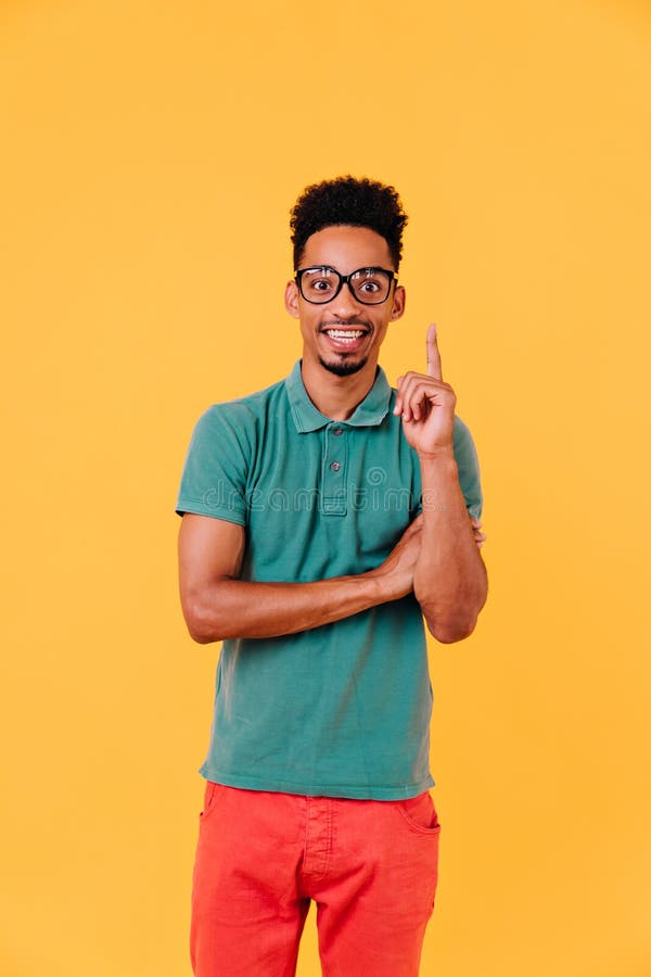 Allegro nero con occhiali giganti che esprime emozioni positive. foto in interni di un elegante uomo africano immagine stock