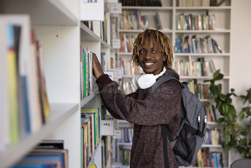 Allegro studente di colore soddisfatto che sceglie un libro di testo sullo scaffale fotografia stock