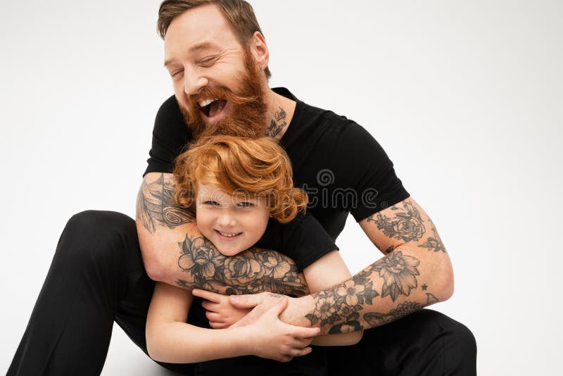 Allegro uomo tatuato con gli occhi chiusi. Uomini allegri tatuati con gli occhi chiusi che abbracciano il nipotino rosso felice con l'immagine di fondo grigio