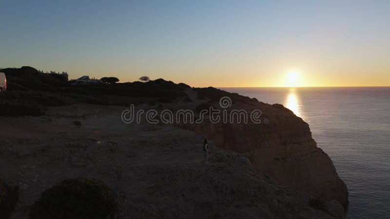 Alleinreisende, die auf steilen Felsen von algarve portugal stehen und beim ruhigen Sonnenuntergang über dem weiten OzeanHorizont stock footage
