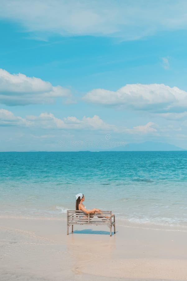 Alleinstehende Frau, die auf einem Stuhl sitzt und den Blick auf den blauen Ozean am Strand genießt. Reise- und Sommerurlaubsfotos lizenzfreie stockfotos