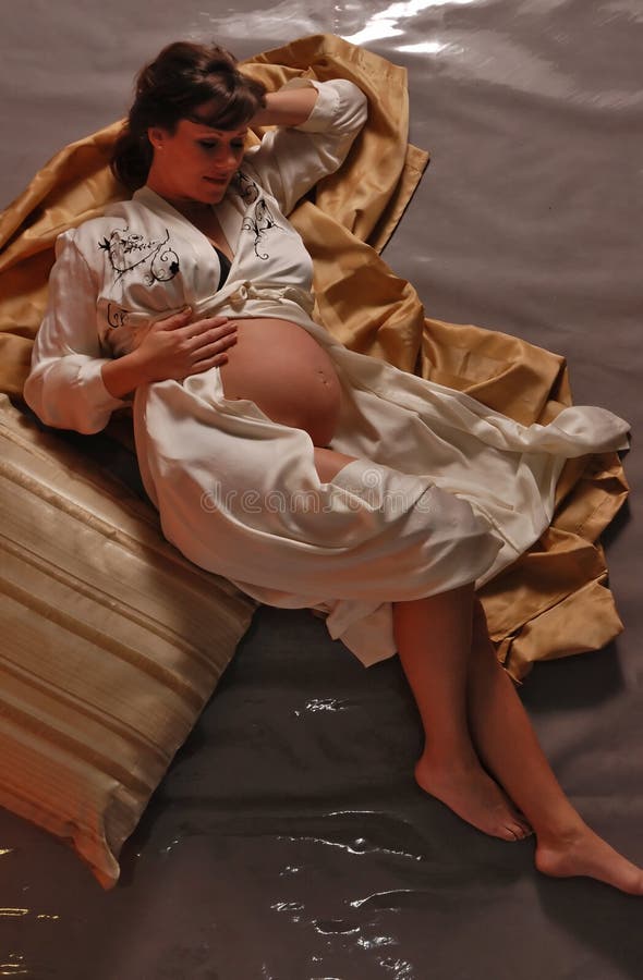 Pregnant woman in cream silk robe looking at her belly with a look of anticipation. Pregnant woman in cream silk robe looking at her belly with a look of anticipation