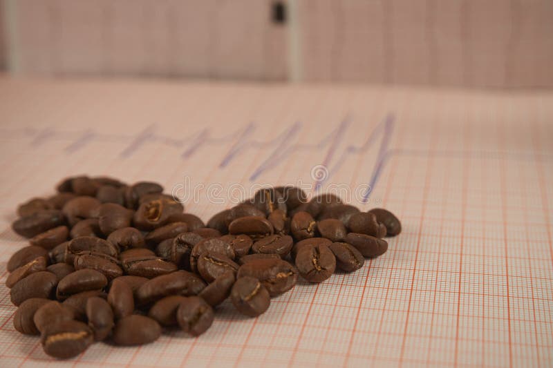 Allenti i chicchi di caffè arrostiti su un tracciato di ECG fotografie stock libere da diritti Allenti i chicchi di caffè arrostiti su un tracciato di ECG fotografie stock libere da diritti